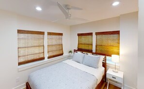 Une chambre à coucher avec un lit, une table de chevet, une lampe et des stores aux fenêtres.