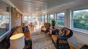 A spacious room with a high ceiling, large windows, and a central seating area with a table and chairs. - Lucky Tern - Ocracoke Island (Ocracoke)