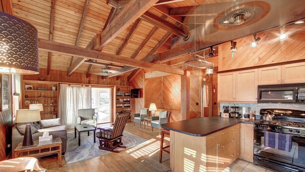 A spacious living area with a fireplace, wooden ceiling beams, and a kitchen with modern appliances. - Lucky Tern - Ocracoke Island (Ocracoke)