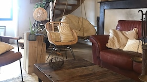 Un salón acogedor con una escalera de madera, un sillón colgante, un sofá rojo y una chimenea.
