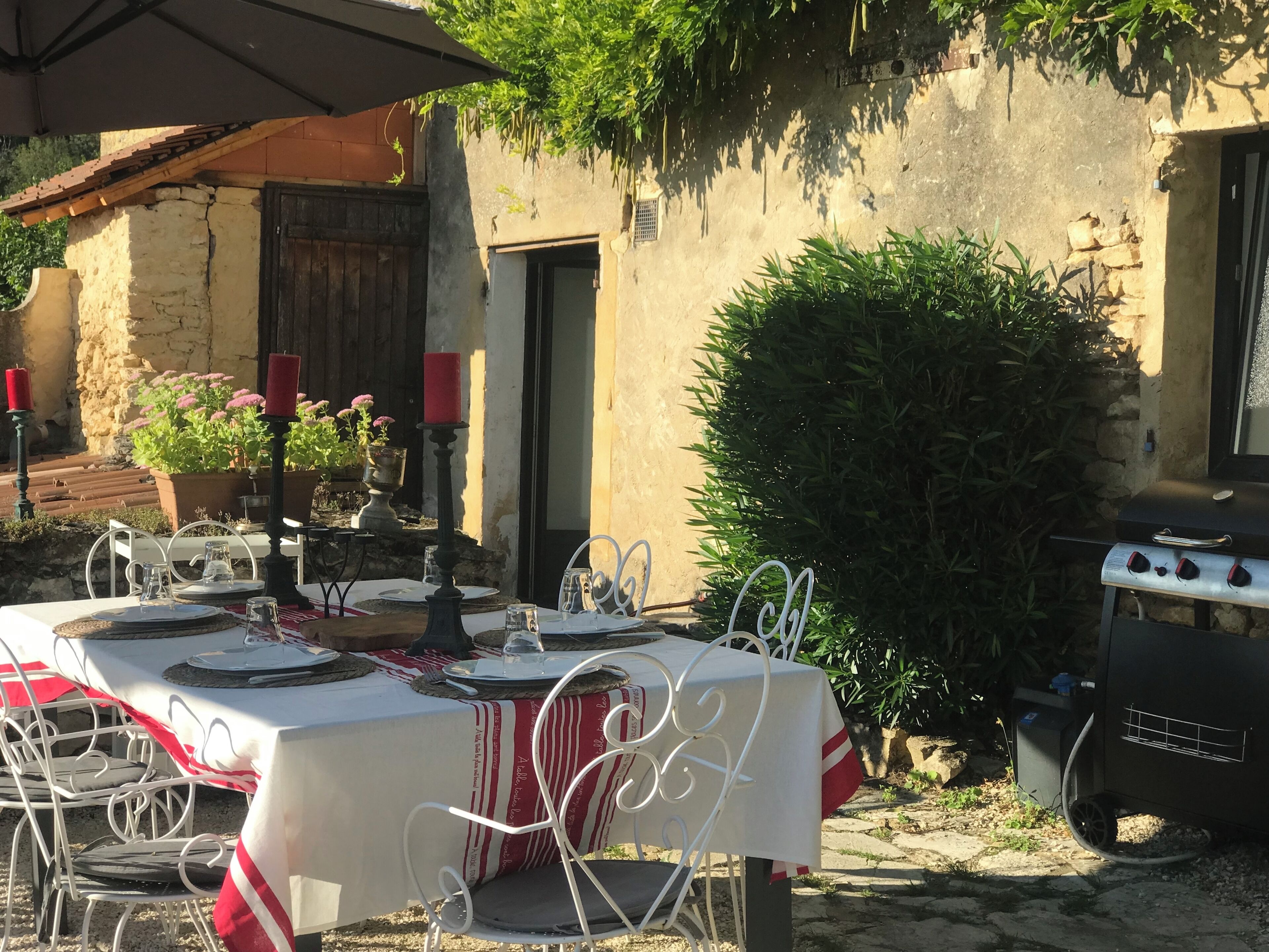 Un espace de restauration en plein air, avec des tables disposées pour deux personnes, entouré de murs en pierre et de verdure.