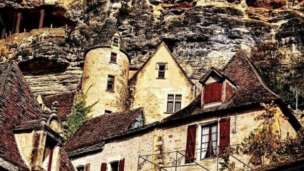 Un edificio histórico de piedra con techo empinado, una pequeña torre y una escalera que conduce a un nivel inferior.