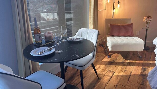 En spiseplads med et rundt bord, hvide stole, en vinflaske og en kage på bordet.