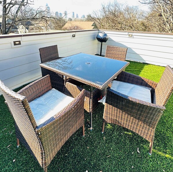 A patio with a glass-top table and wicker chairs, surrounded by a white fence and a grassy area. - Tiny Space, Tons of Fun (Charlotte)