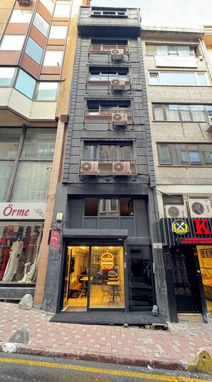 Ein Gebäude mit Restaurant im Erdgeschoss, mit leuchtendem Neon-Burger-Schild, mehreren Klimaanlagen und einem gut sichtbaren Eingang mit Glastür.