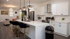 A modern kitchen with white cabinetry, stainless steel appliances, and a central island with bar stools. - ATL Getaway • 10 Min to Downtown & Benz (Atlanta)