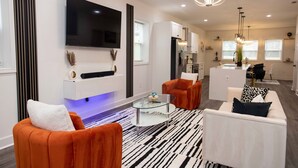 A modern living room with a flat-screen TV, orange and white furniture, a glass coffee table, and a patterned rug. - ATL Getaway • 10 Min to Downtown & Benz (Atlanta)