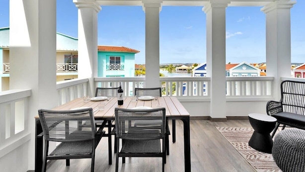 A covered outdoor dining area with a wooden table and chairs, a patterned rug, and a view of colorful buildings. - Kas Ariba with pool and Laguna Marina View (Kralendijk)