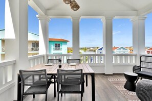 A covered outdoor dining area with a wooden table and chairs, a patterned rug, and a view of colorful buildings. - Kas Ariba with pool and Laguna Marina View (Kralendijk)
