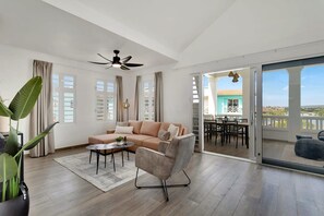 A spacious living area with a sofa, armchair, and coffee table, a ceiling fan, and a view of a balcony with outdoor furniture. - Kas Ariba with pool and Laguna Marina View (Kralendijk)