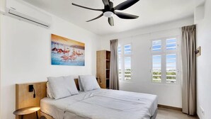 A bedroom with a bed, a ceiling fan, a painting, a window with curtains, and a wooden cabinet. - Kas Ariba with pool and Laguna Marina View (Kralendijk)