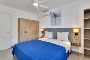A hotel room with a bed, a ceiling fan, a wall-mounted air conditioner, a painting of a flamingo, and a wooden wardrobe. - Kavel 17 - Turtles Place with a refreshing shared pool in the heart of Kralendijk (Kralendijk)
