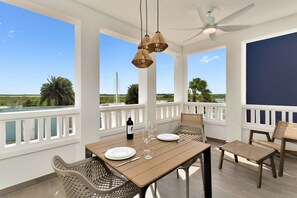En balkon med et træbord dækket til spisning, fletstole og udsigt over landskabet.
