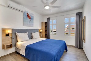 Et hotelværelse med en seng, en ventilator i loftet, et vindue med gardiner og et maleri af en flamingo.