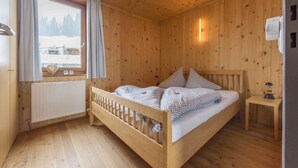 Une chambre dans une cabane en bois, avec un lit, une fenêtre avec des rideaux, un radiateur et une petite table de chevet.