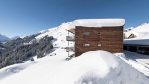 Un bâtiment moderne en bois, doté d’un balcon, entouré de montagnes et d’arbres couverts de neige.