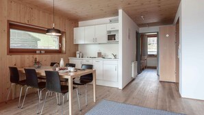 Une cuisine moderne avec des meubles blancs, un four à micro-ondes et un coin repas comprenant une table et des chaises en bois.