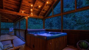 Una cabaña de madera con jacuzzi, terraza de madera y grandes ventanales con vistas a un bosque.