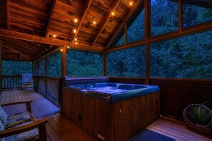 Una baita in legno con idromassaggio, terrazza in legno e ampie finestre affacciate su una foresta.