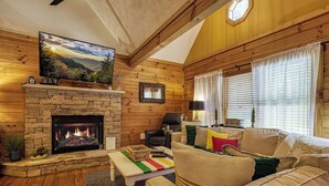 Una sala de estar acogedora con una chimenea de piedra, paredes de madera, un sofá cómodo y un televisor sobre la chimenea.