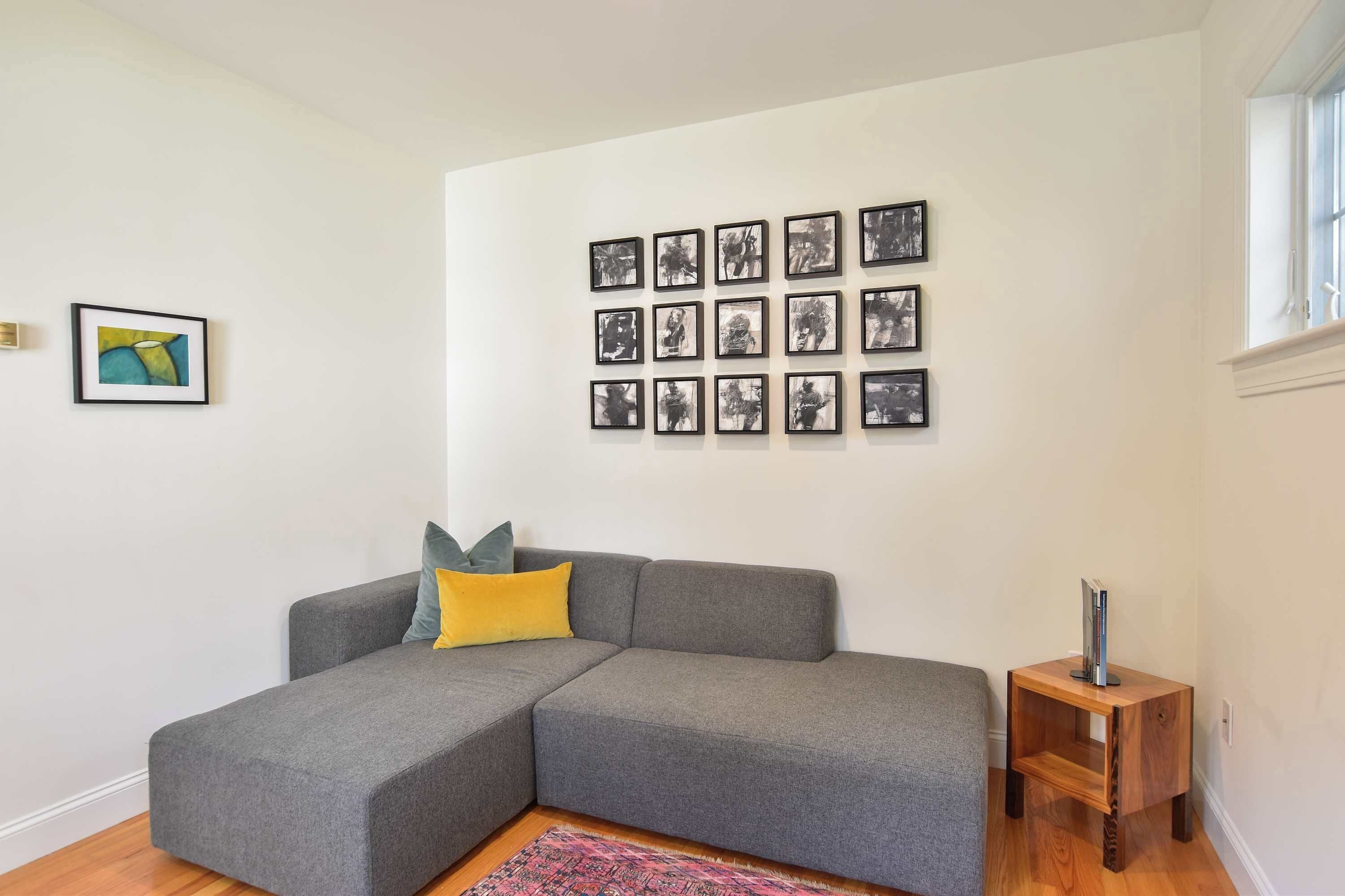 Een woonkamer met een grijze modulaire bank, een klein houten bijzettafeltje en een muur met meerdere ingelijste foto's.