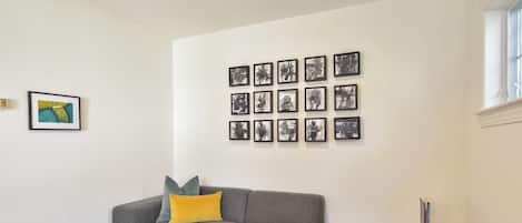 Een woonkamer met een grijze modulaire bank, een klein houten bijzettafeltje en een muur met meerdere ingelijste foto's.