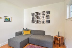 A living room with a grey sectional sofa, a small wooden side table, and a wall with multiple framed pictures.