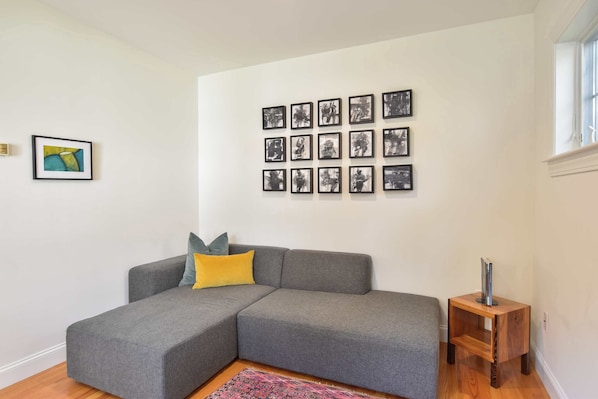 A living room with a grey sectional sofa, a small wooden side table, and a wall with multiple framed pictures. - Perfectly private location w/deeded beach access! (Orleans)