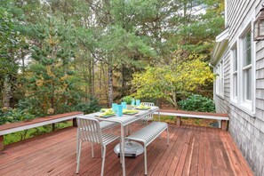 An outdoor deck with a dining table set for four, surrounded by trees and a house.