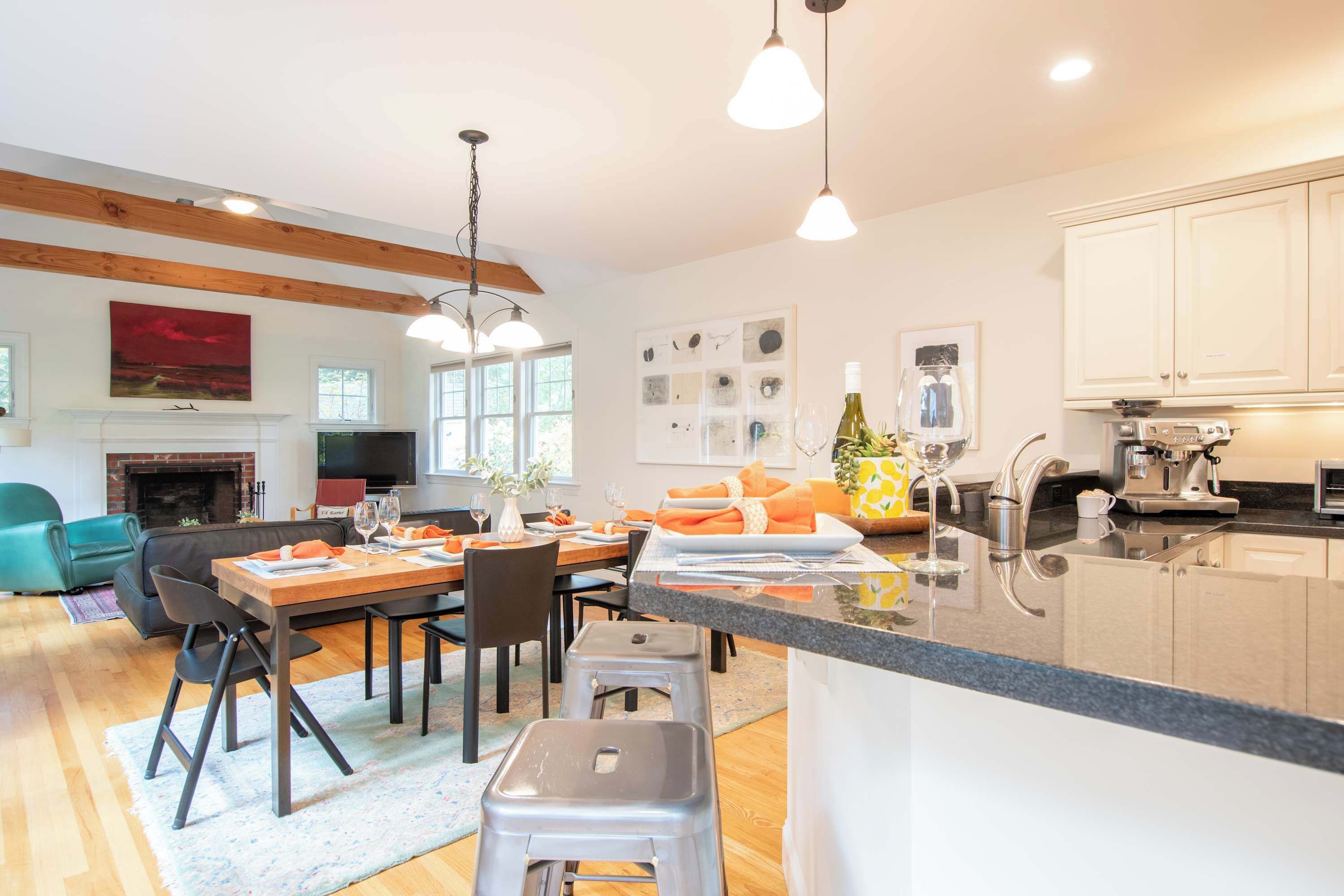 A modern kitchen with a central island, dining area with chairs and table, and a living room with a sofa and fireplace.