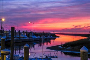 A marina at sunset with boats docked, a pier, and calm water reflecting the sky.