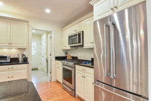 A modern kitchen with stainless steel appliances, white cabinetry, and a wooden floor. - Perfectly private location w/deeded beach access! (Orleans)
