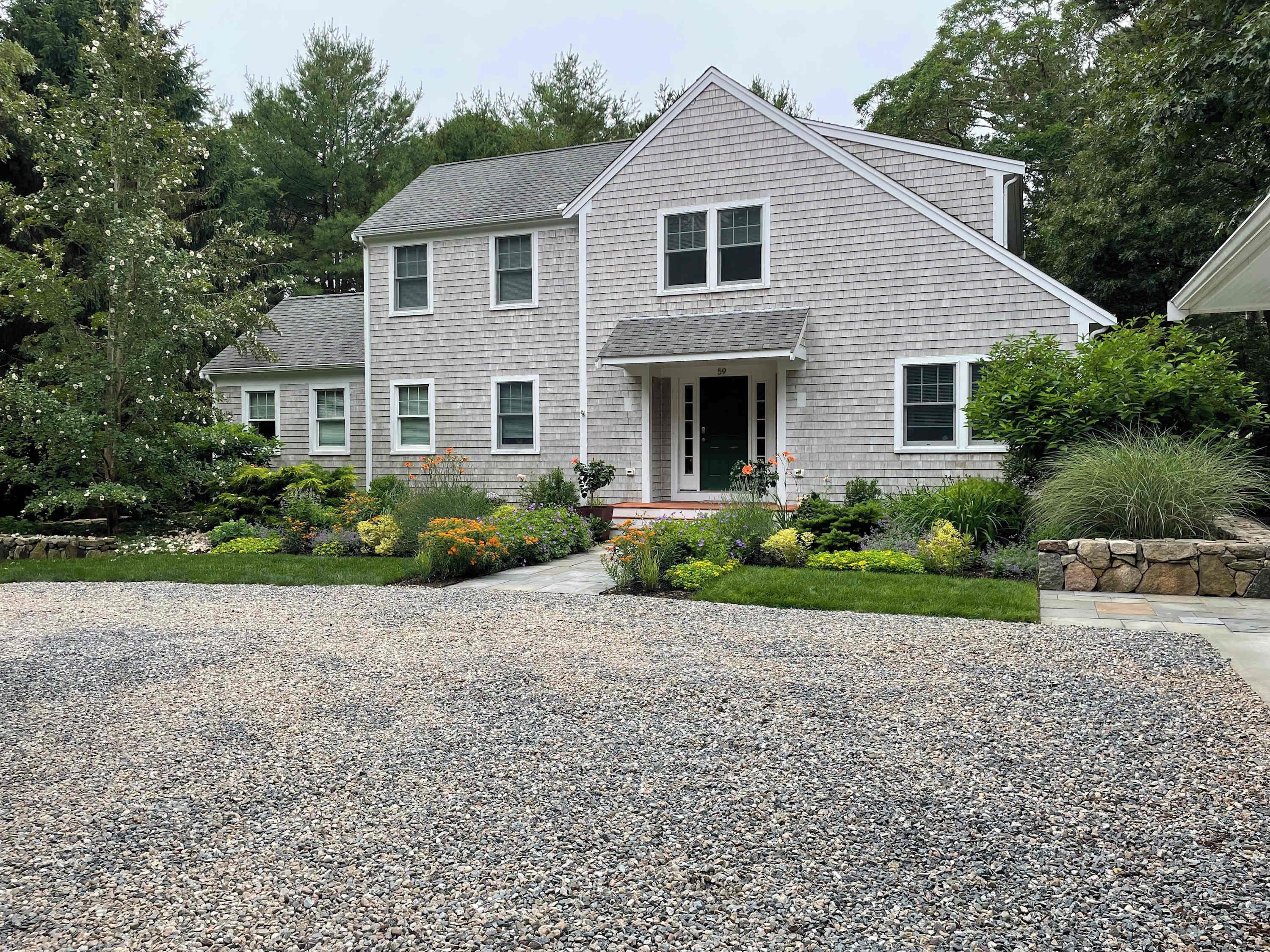A two-story house with a gravel driveway and a well-maintained garden.
