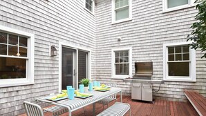 A patio with a table set for dining, a grill, and a bench.