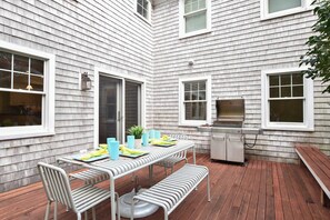 A patio with a table set for dining, a grill, and a bench.