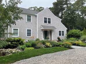 A two-story house with a front porch, surrounded by a well-maintained garden with various plants and flowers. - Perfectly private location w/deeded beach access! (Orleans)