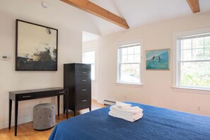 A bedroom with a bed, a desk, a dresser, and a painting on the wall.