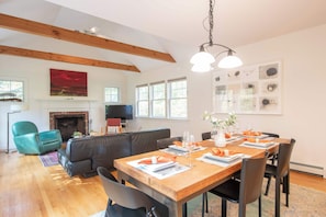A spacious living area with a fireplace, a dining table set for six, and a large window providing natural light. - Perfectly private location w/deeded beach access! (Orleans)