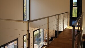 Ein großzügiger Innenraum mit hoher Decke, einer Treppe mit Glasgeländern und Blick auf einen Garten durch eine Tür.