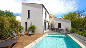 Ein modernes Haus mit Swimmingpool, Liegestühlen und einer Terrasse.