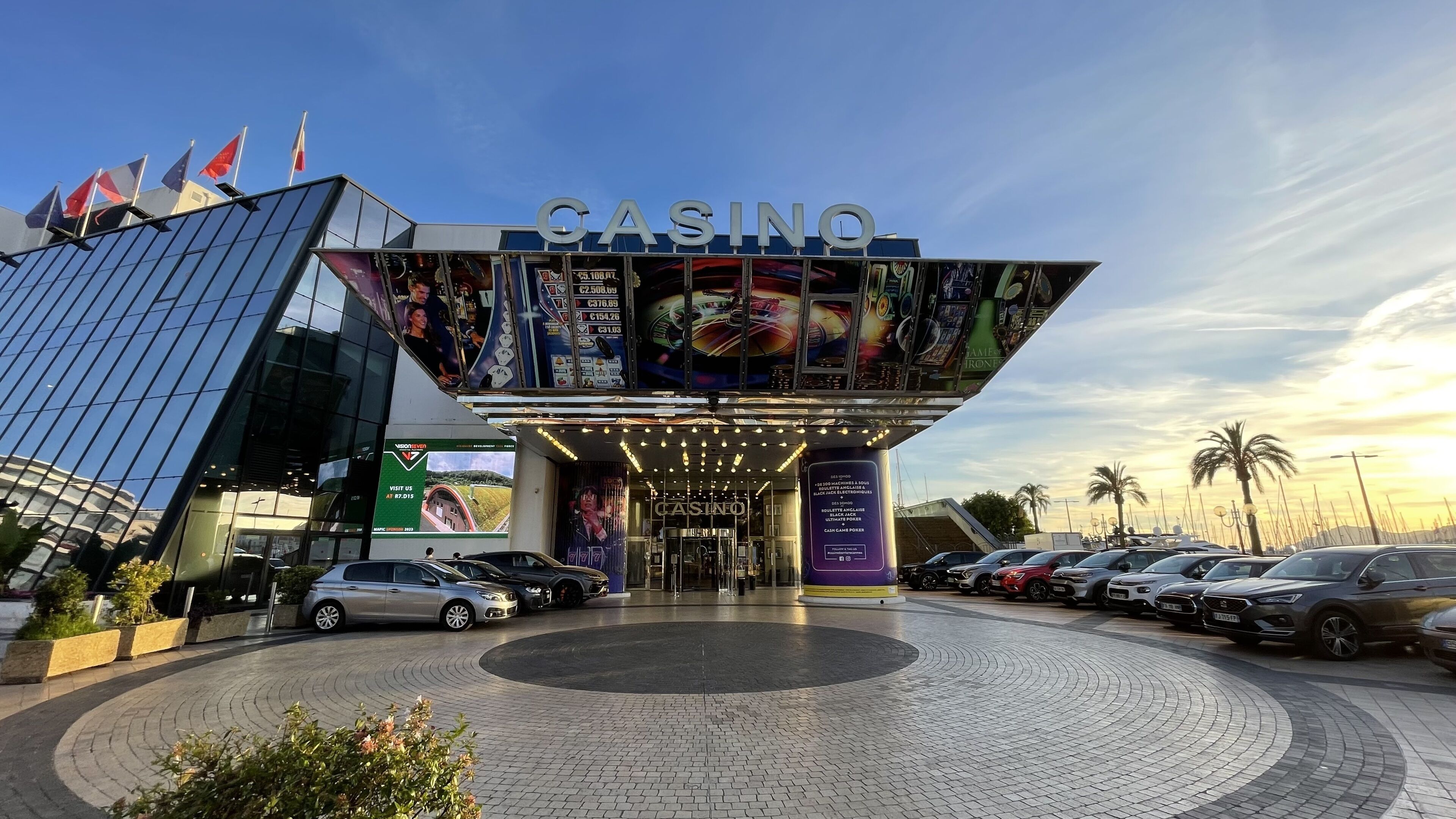 Een casino met een moderne glazen gevel, een ruime entree en een parkeerplaats met meerdere auto's.