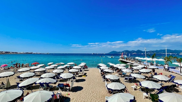 A beach with rows of umbrellas and chairs, a pier extending into the sea, and boats in the background. - Comfortable studio near the beaches (Cannes)