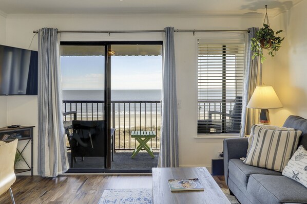 Un salon comprenant un canapé, une table basse, un téléviseur et un balcon avec vue sur la plage.