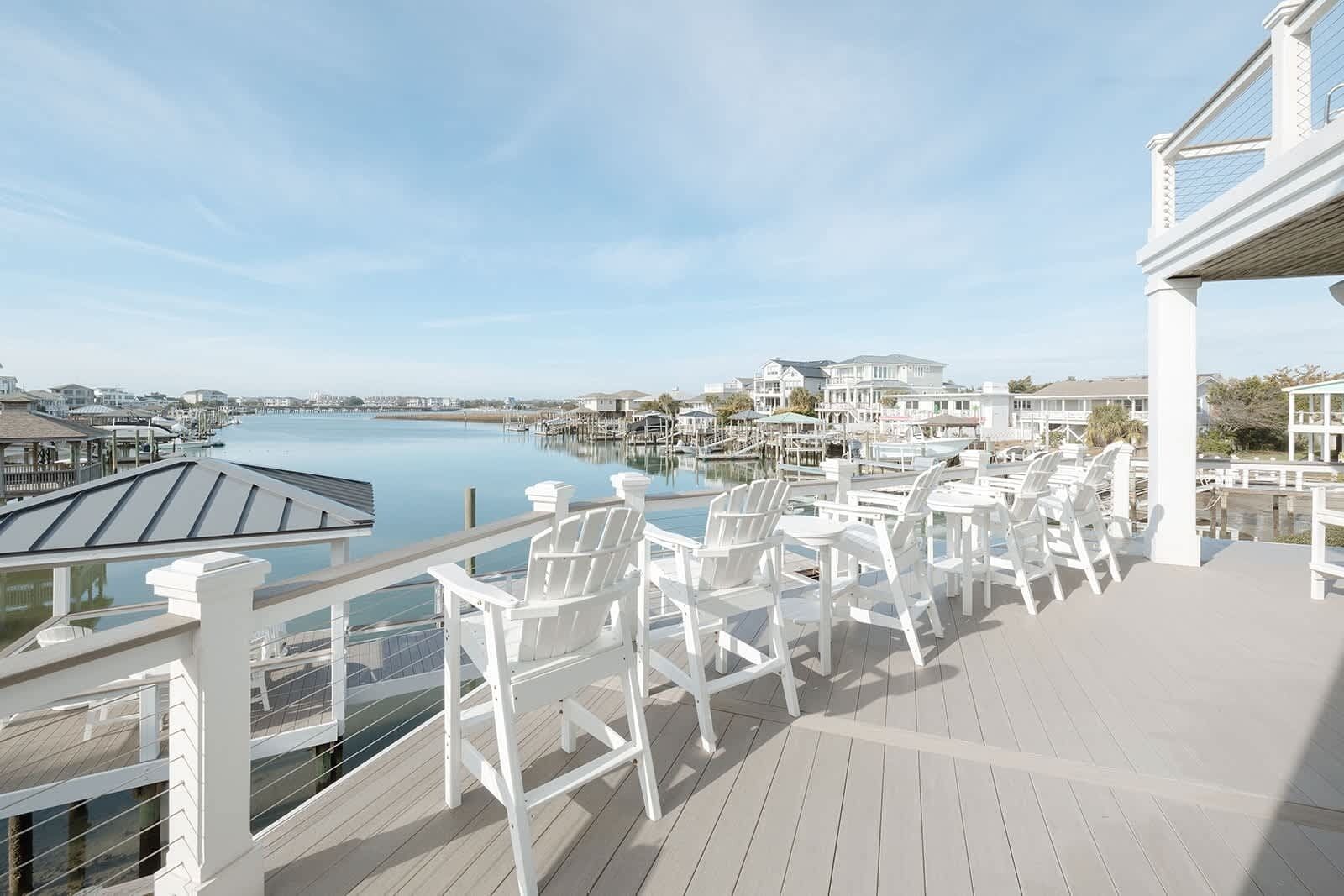 A deck with white chairs overlooking a marina and waterfront houses.