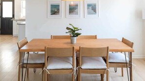 A dining area with a wooden table, six chairs, a hanging light fixture, and three framed pictures on the wall.