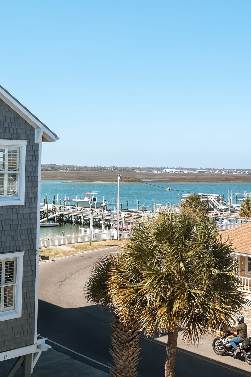 A coastal view with a marina, a house with a balcony, and a palm tree.