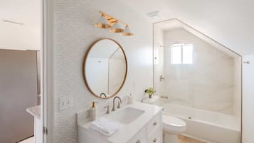 A modern bathroom with a freestanding bathtub, a round mirror, and a vanity with a sink and towel.