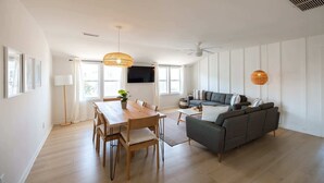 A modern living room with a dining area, a grey sofa, and a flat-screen TV mounted on the wall.