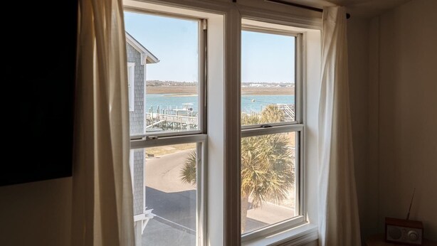 A room with a large window overlooking a beach and a dock.