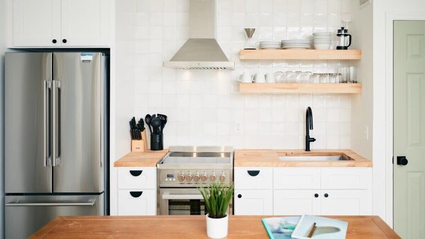 Una cocina moderna con electrodomésticos de acero inoxidable, encimeras de madera y armarios blancos.